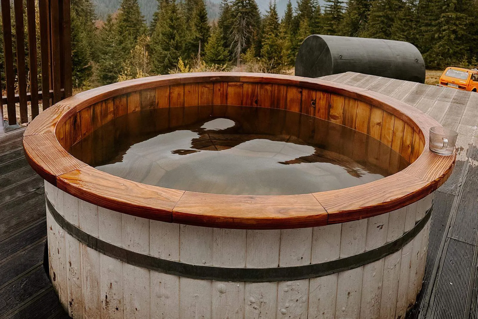 A round wooden tub with a cedar rim, filled with water, on a deck above a forest valley.